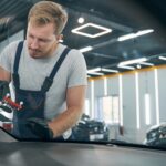 Man repair crack on car windshield. Restoring front window in workshop